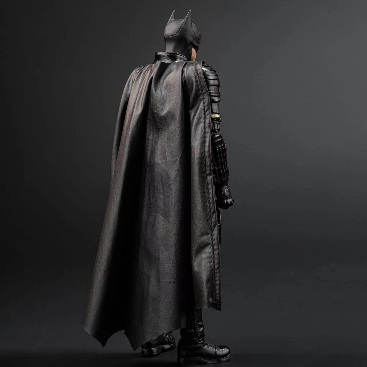 Dark armored Batman figure in black cape and helmet standing against gray background