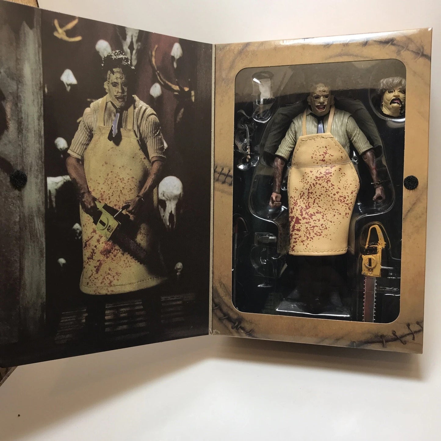 Leatherface action figure with blood-stained yellow apron, chainsaw, and extra head in collectible horror packaging