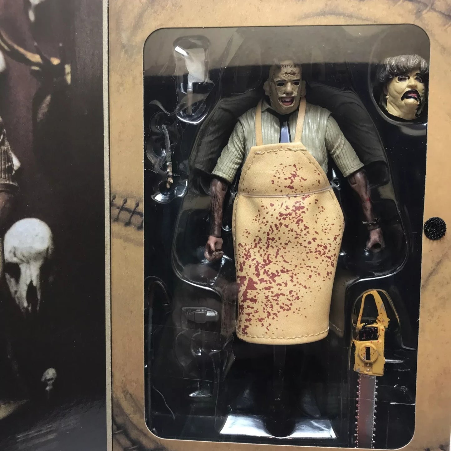 Leatherface horror figure in blood-spattered apron with chainsaw and alternate head in packaging