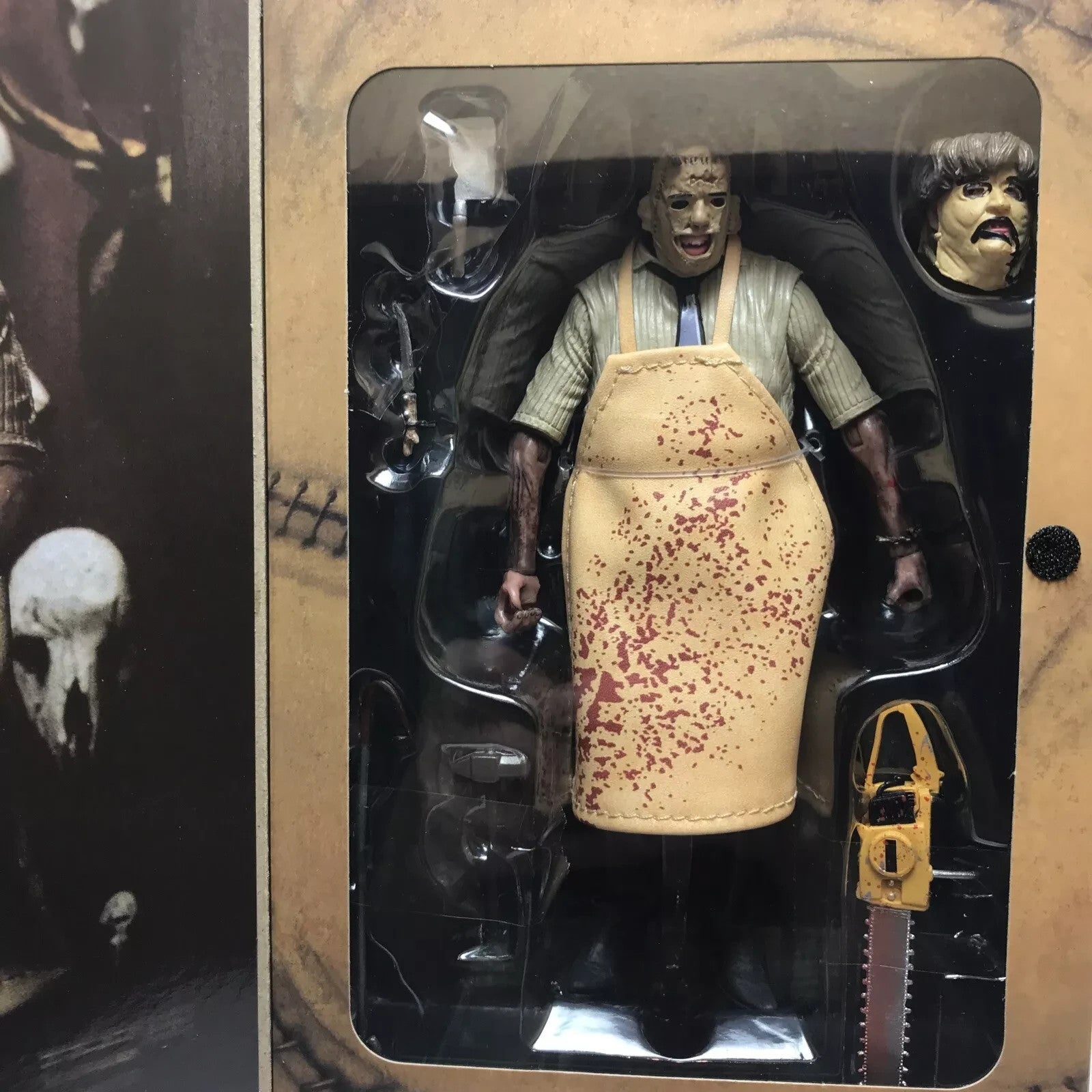 Leatherface horror figure in blood-spattered apron with chainsaw and alternate head in packaging