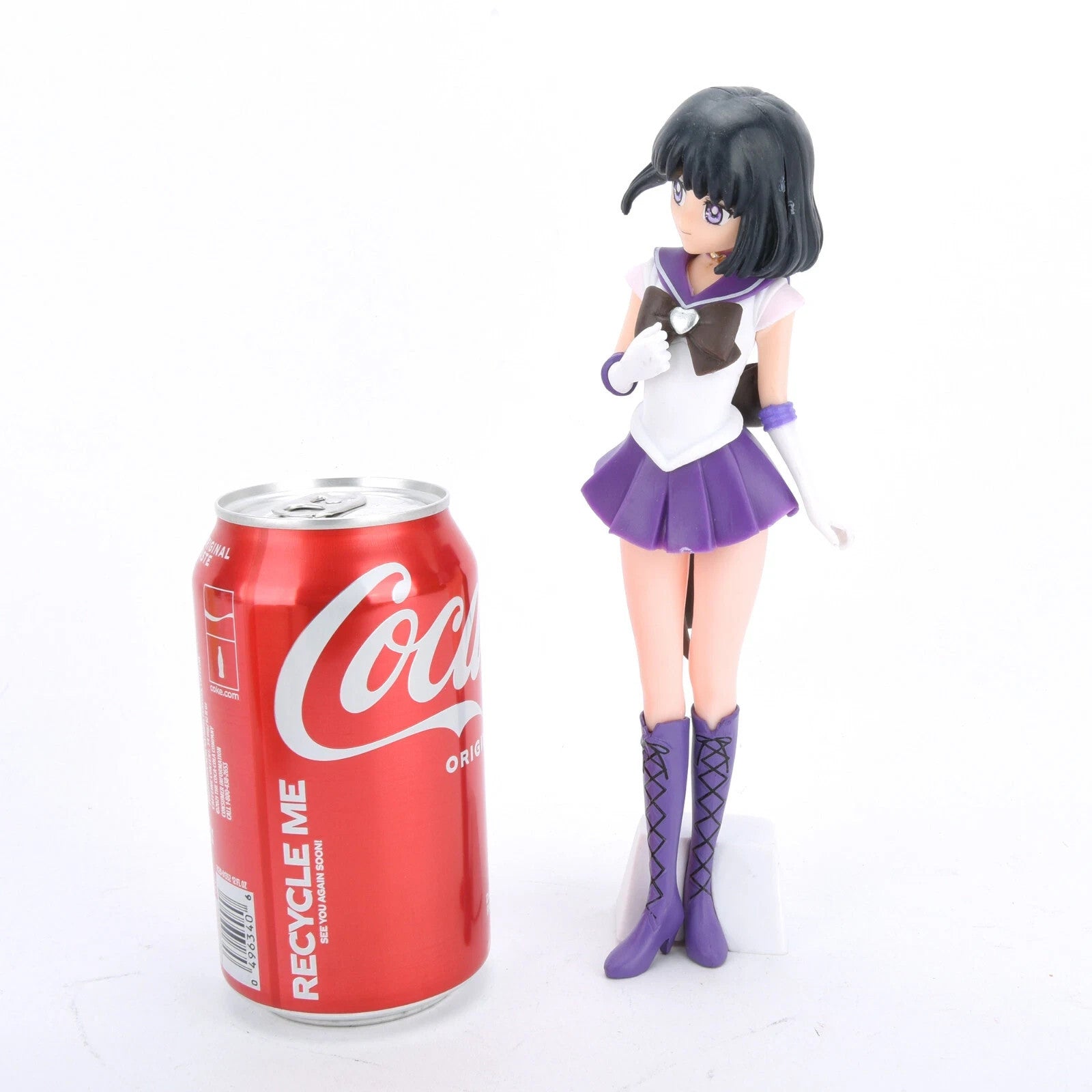Purple and white anime figurine standing next to a red Coca-Cola can on white background