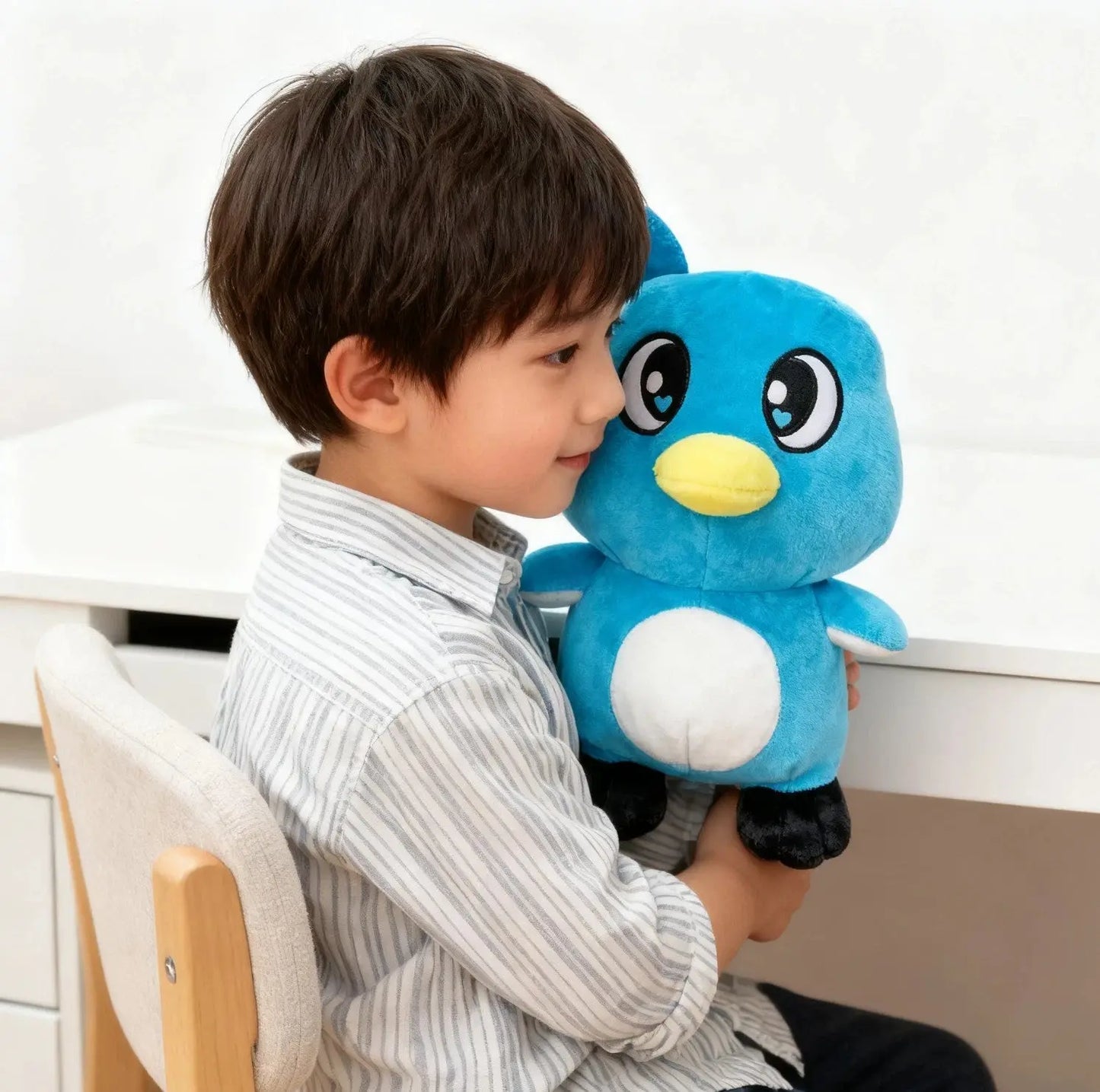 Child sitting on chair hugging a blue penguin plush toy with big eyes and yellow beak