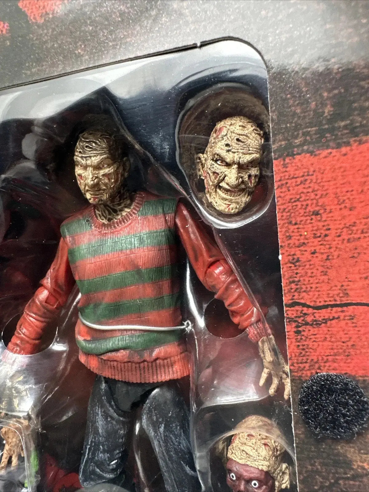 Freddy Krueger horror action figure with striped sweater and two interchangeable bloody zombie heads in packaging